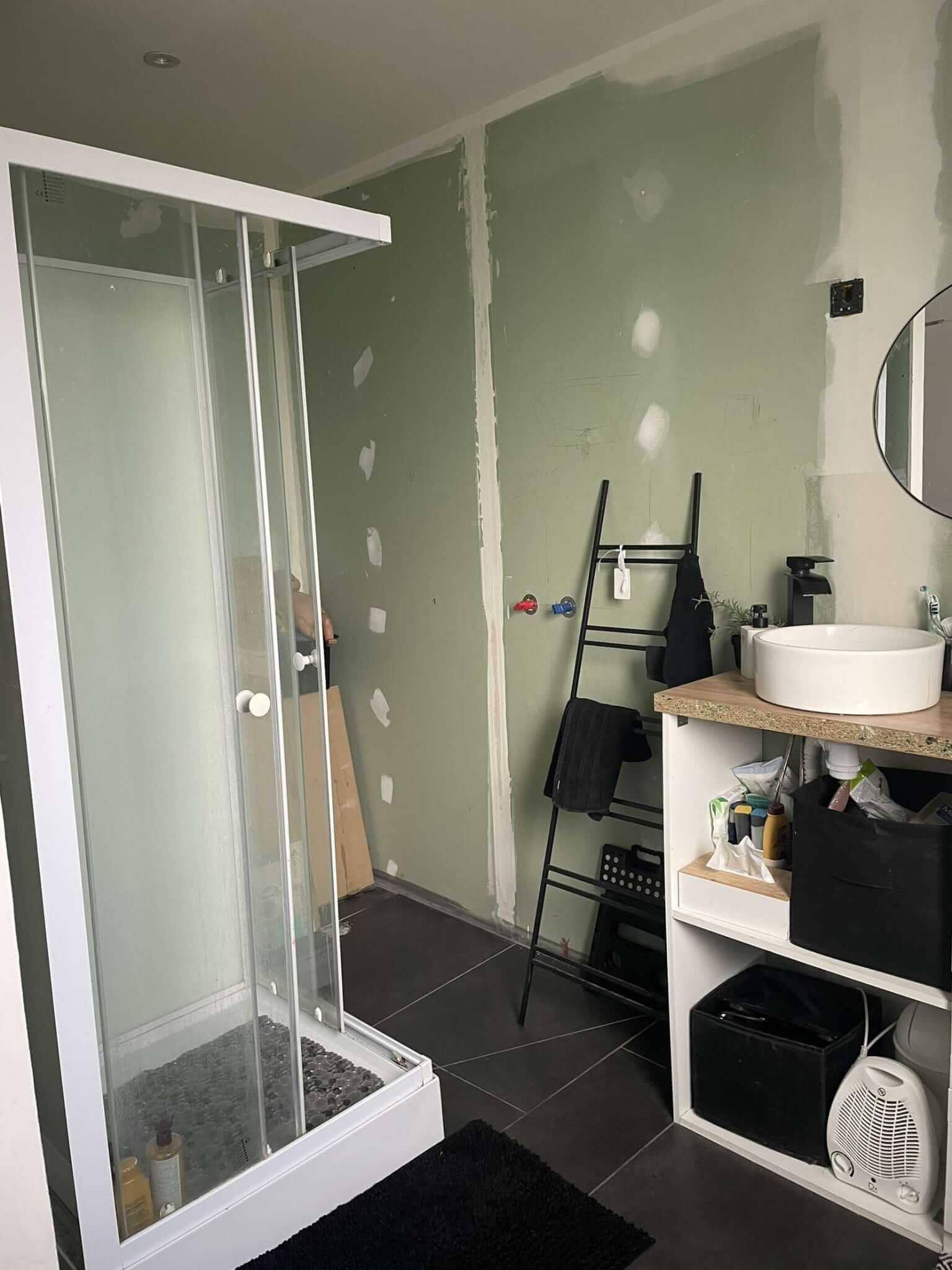La pièce au premier passage : cabine de douche, murs bruts et meuble vasque en bout.
